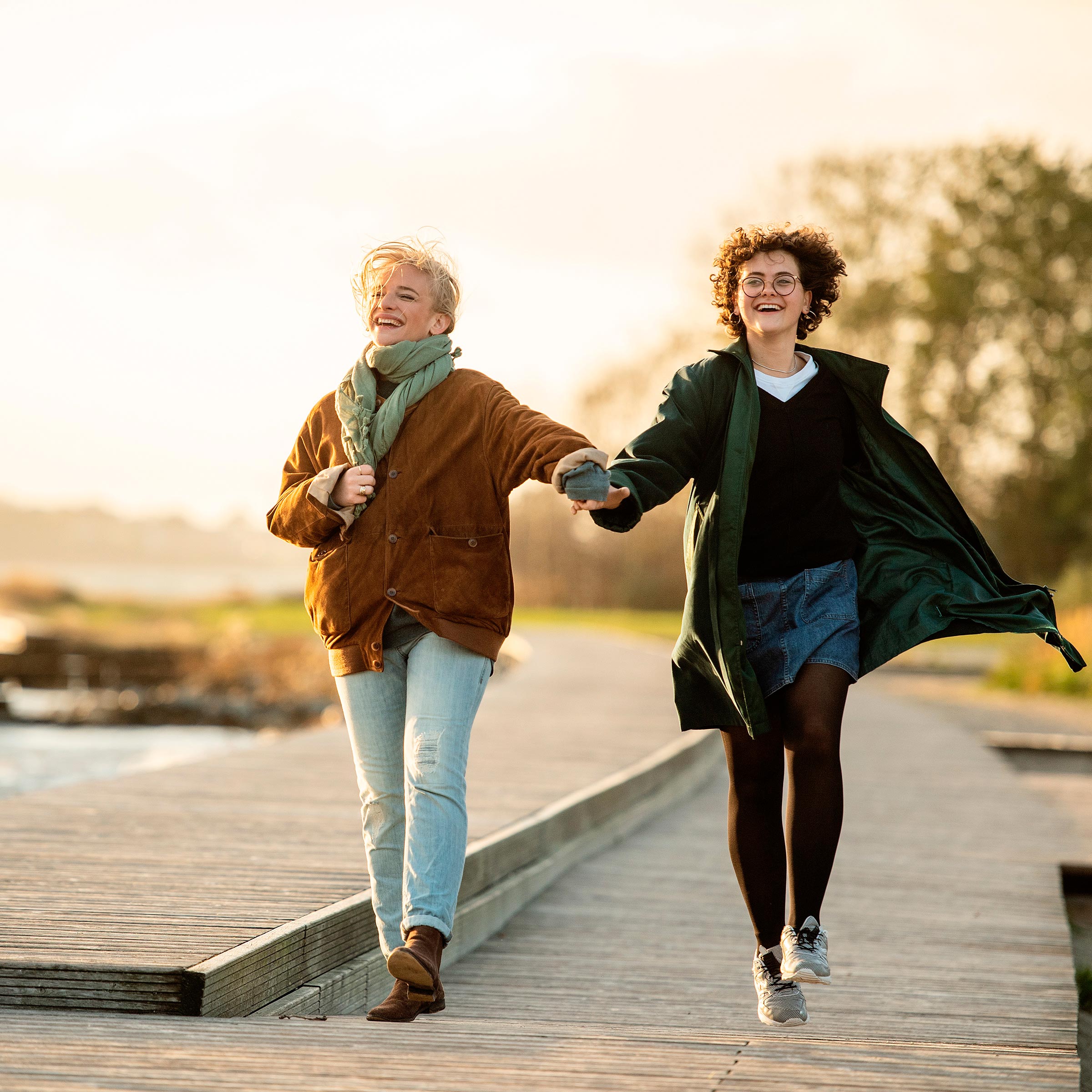 Due persone che camminano mano nella mano su un lungomare vicino all’acqua alla luce soffusa del sole.