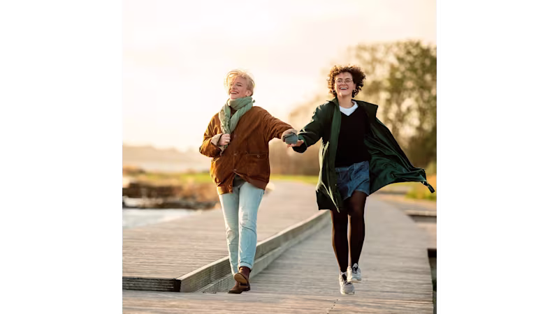 Due persone che camminano mano nella mano su un lungomare vicino all’acqua alla luce soffusa del sole.