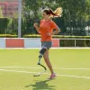 Um atleta amputado se exercita antes de um jogo, correndo levemente em um campo de futebol ao ar livre