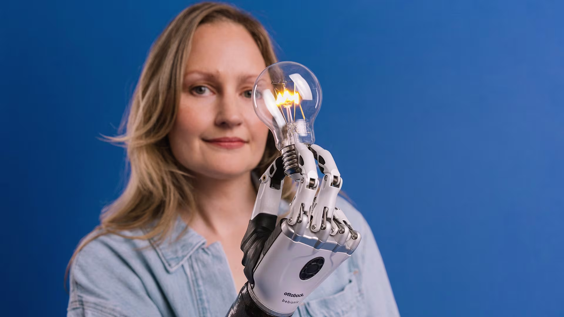 A woman with a bebionic prosthetic hand holding a light bulb.  