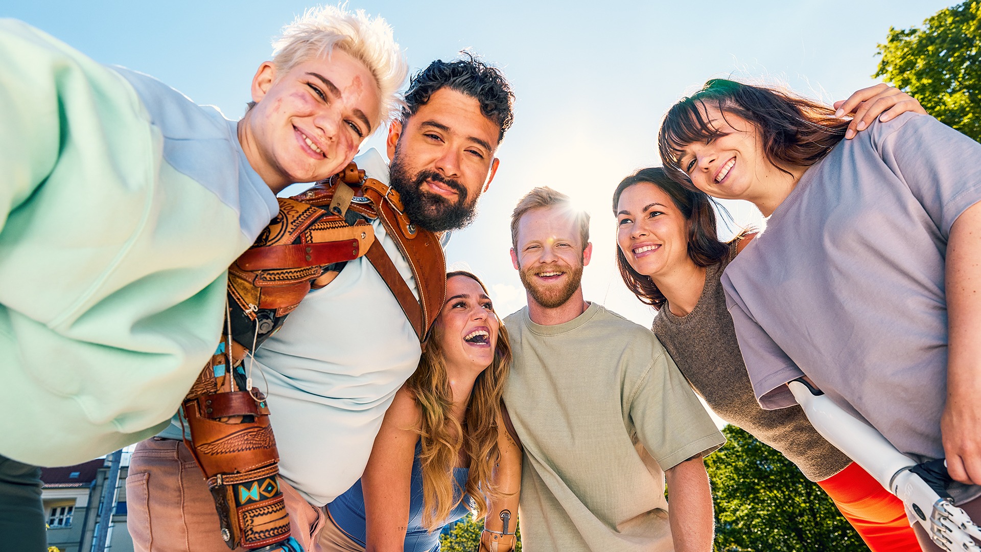 A group consisting of three smiling women and three smiling men, some with prosthetic arms, standing together in a semicircle.