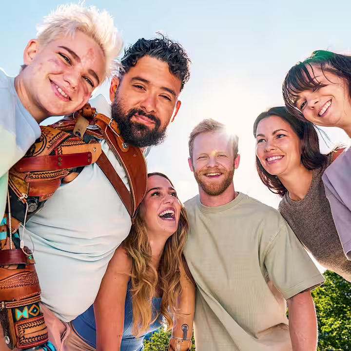 A group consisting of three smiling women and three smiling men, some with prosthetic arms, standing together in a semicircle.