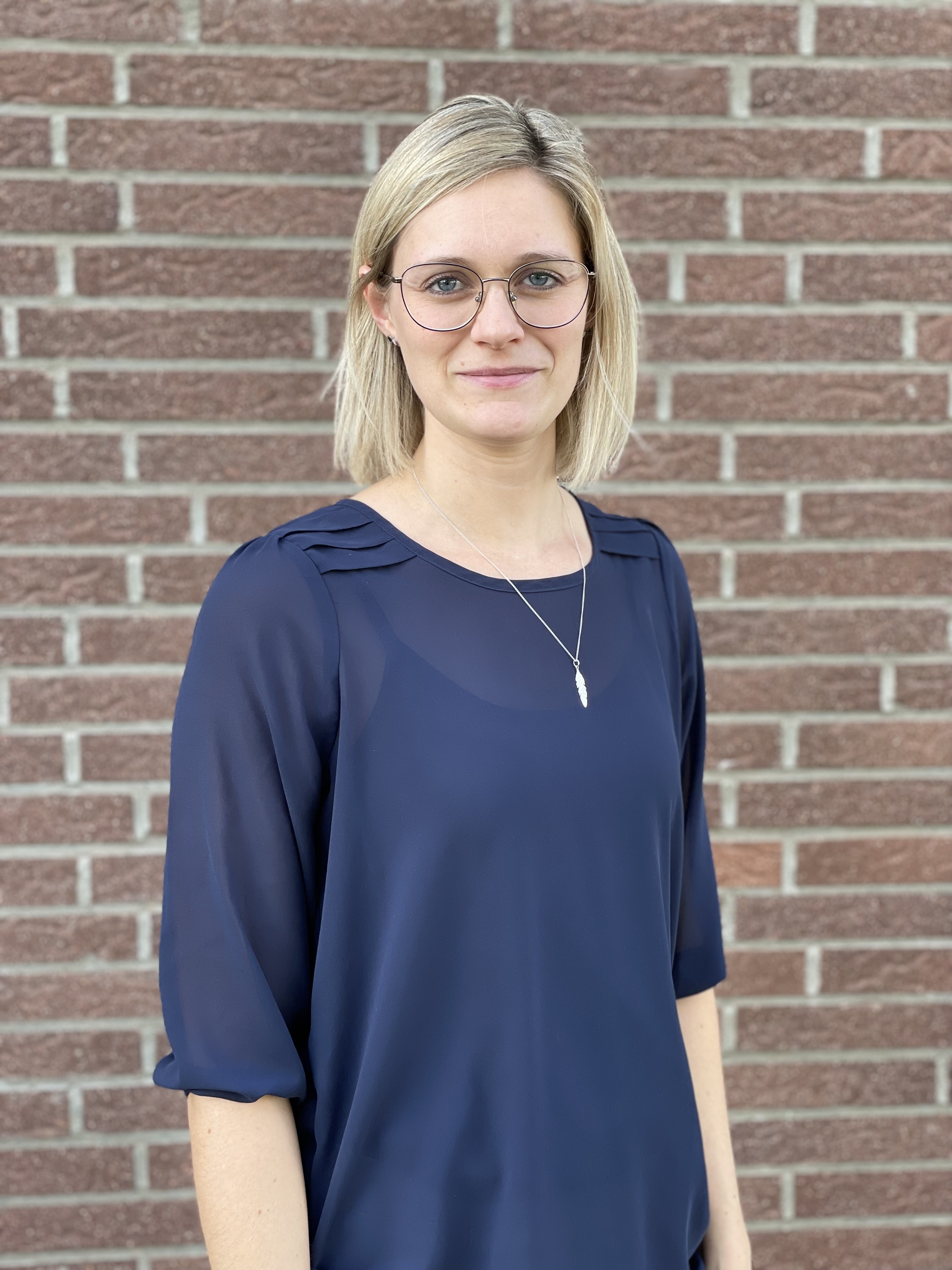 Auf dem Bild ist das Portrait einer Ottobock Academy Mitarbeiterin zu sehen. Sie hat blonde Haare, trägt eine Brille und lacht in die Kamera.