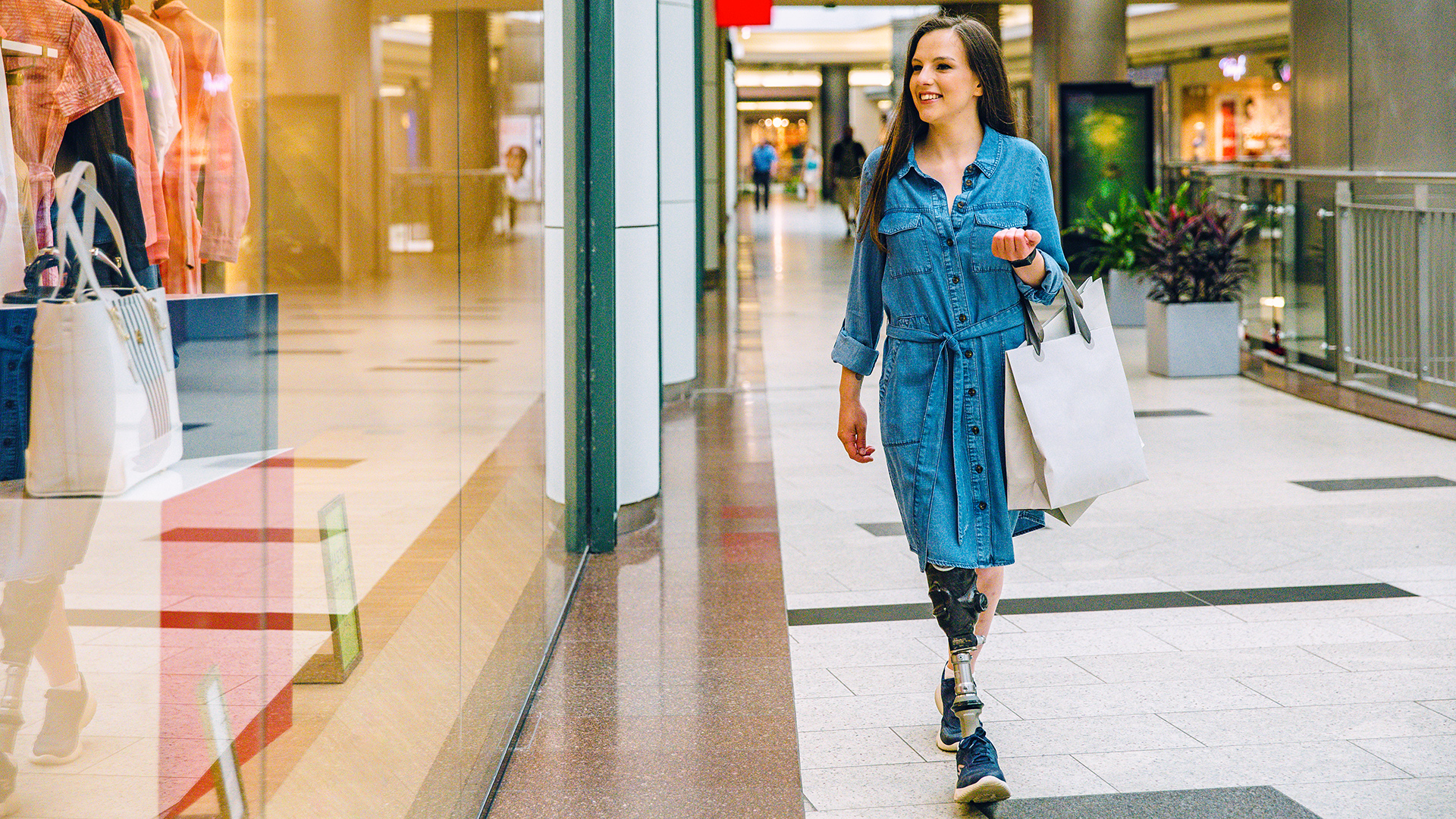 Bir kadın kullanıcı Taleo Vertical Shock ayağıyla yürürken alışveriş poşetlerini giyiyor.