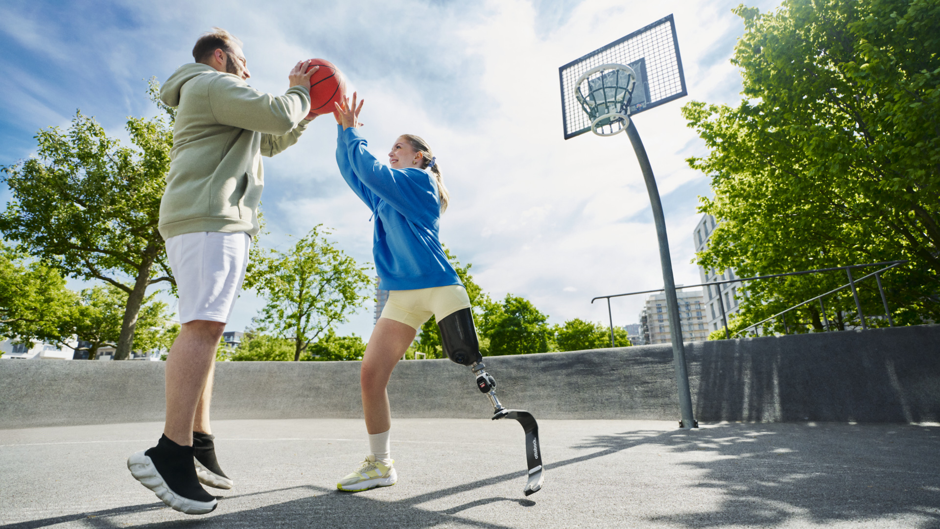 Eine Frau und ein Mann spielen gemeinsam Basketball auf einem Outdoor-Court. Die Frau ist beinamputiert und nutzt eine Sportprothese von Ottobock.