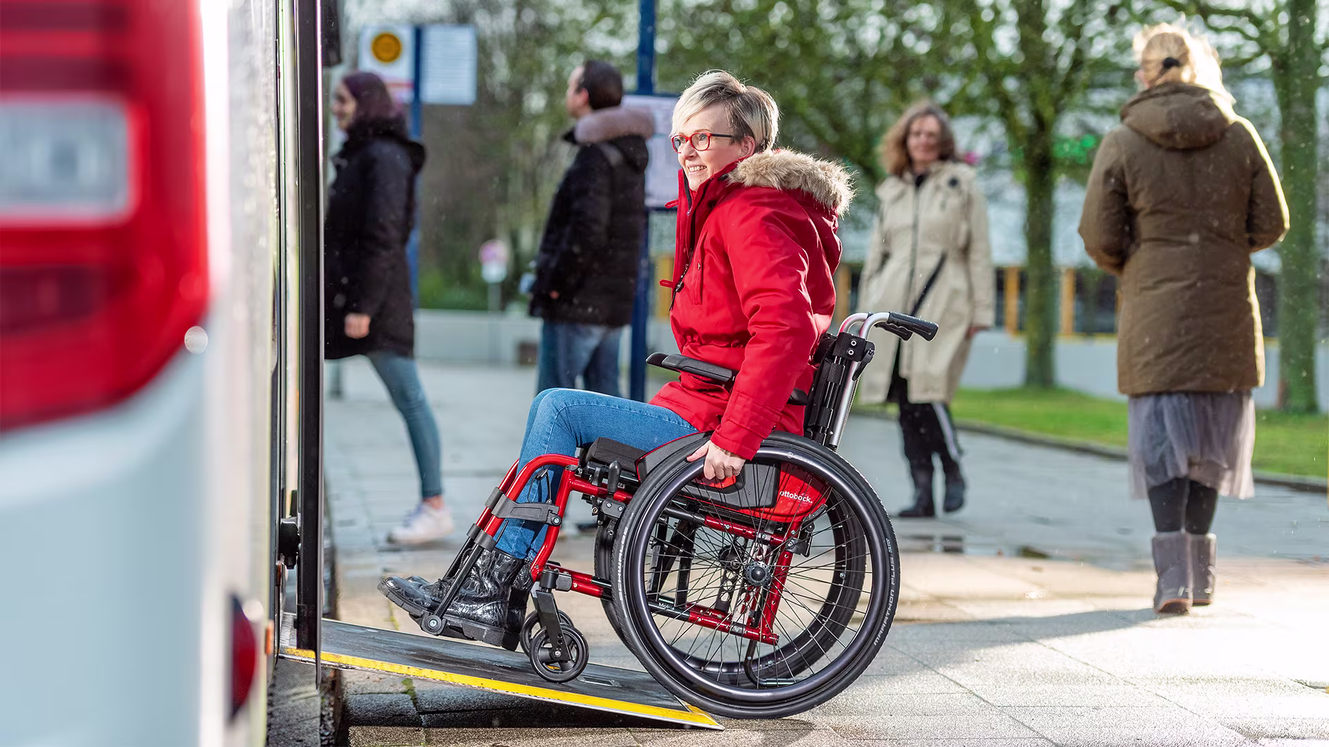Auf dem Bild sieht man eine Frau, die in einem Rollstuhl sitzt. Sie fährt über eine Rampe in einen Bus rein.