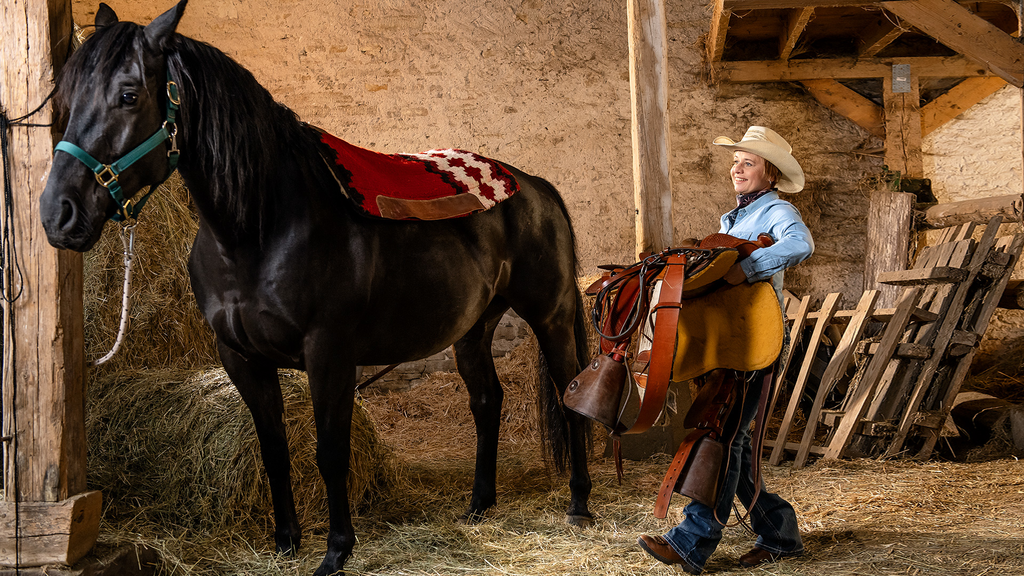 A person with a transtibial amputation carries a saddle toward a horse.