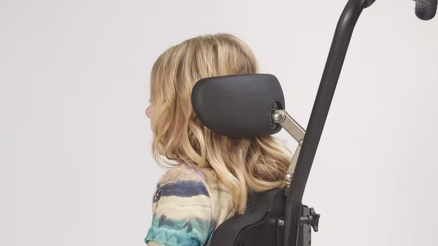 A side view of a young girl in her kidevo wheelchair, focused on the adjustable head support.