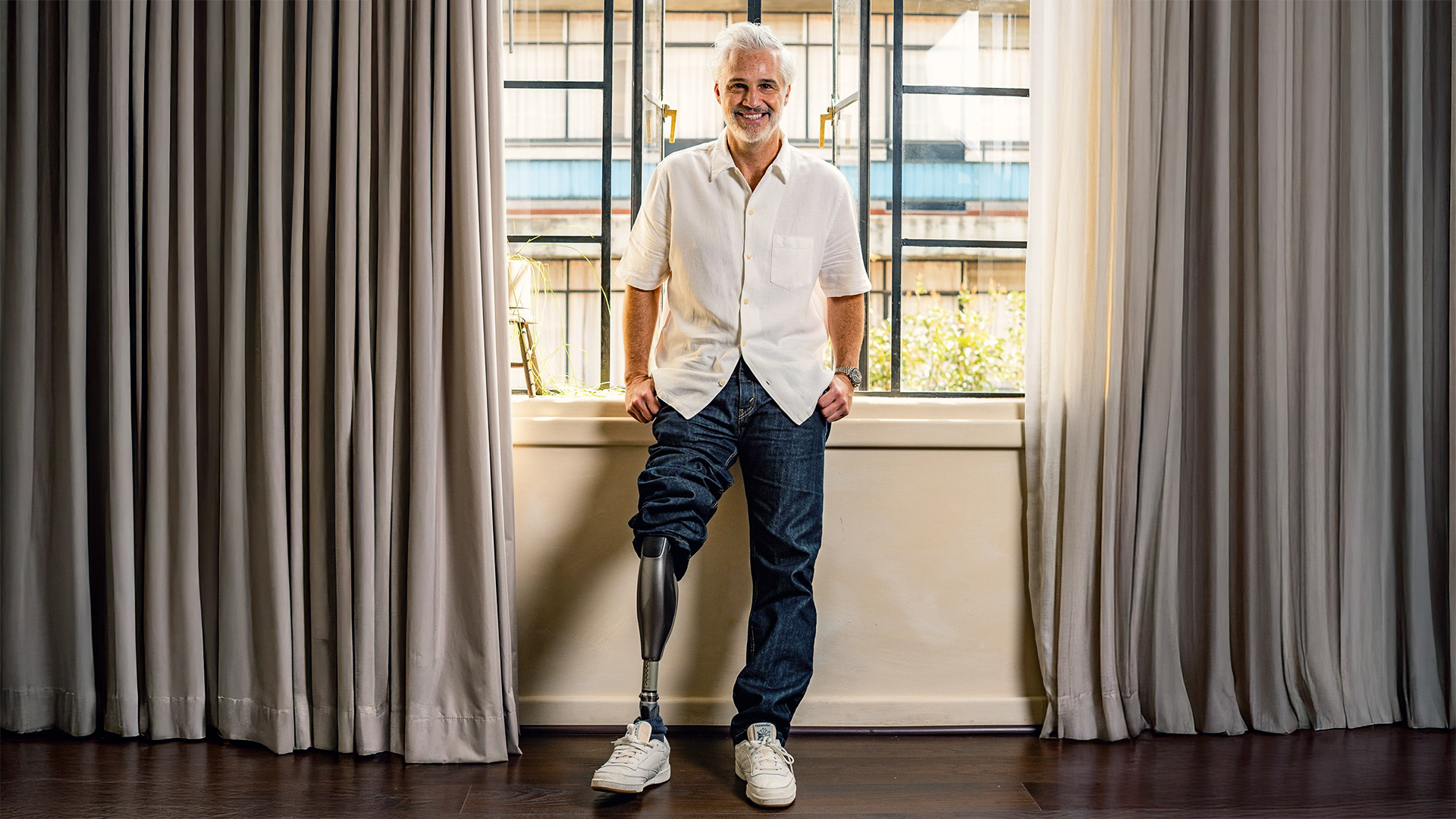 A man with a prosthetic leg stands in front of a window.