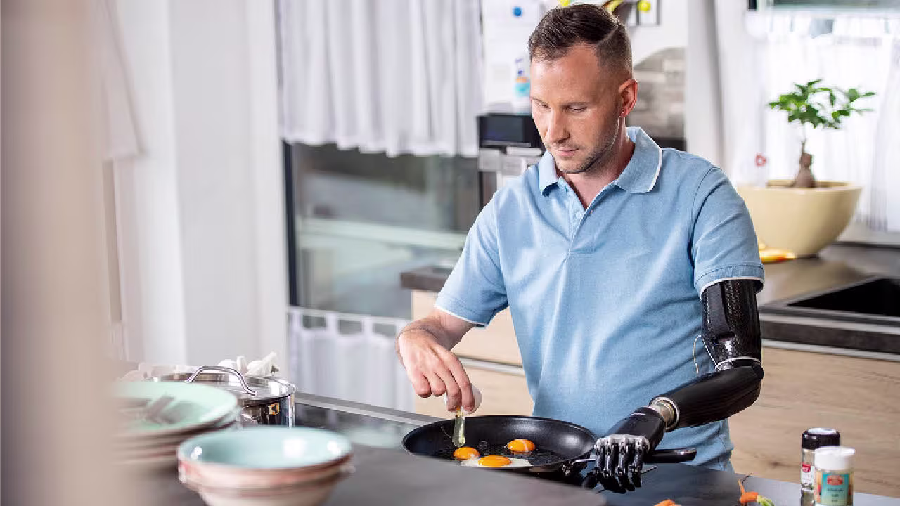 Ein Armprothesenträger steht in der Küche und kocht mit einer Pfanne. Er trägt die bebionic Hand von Ottobock. 