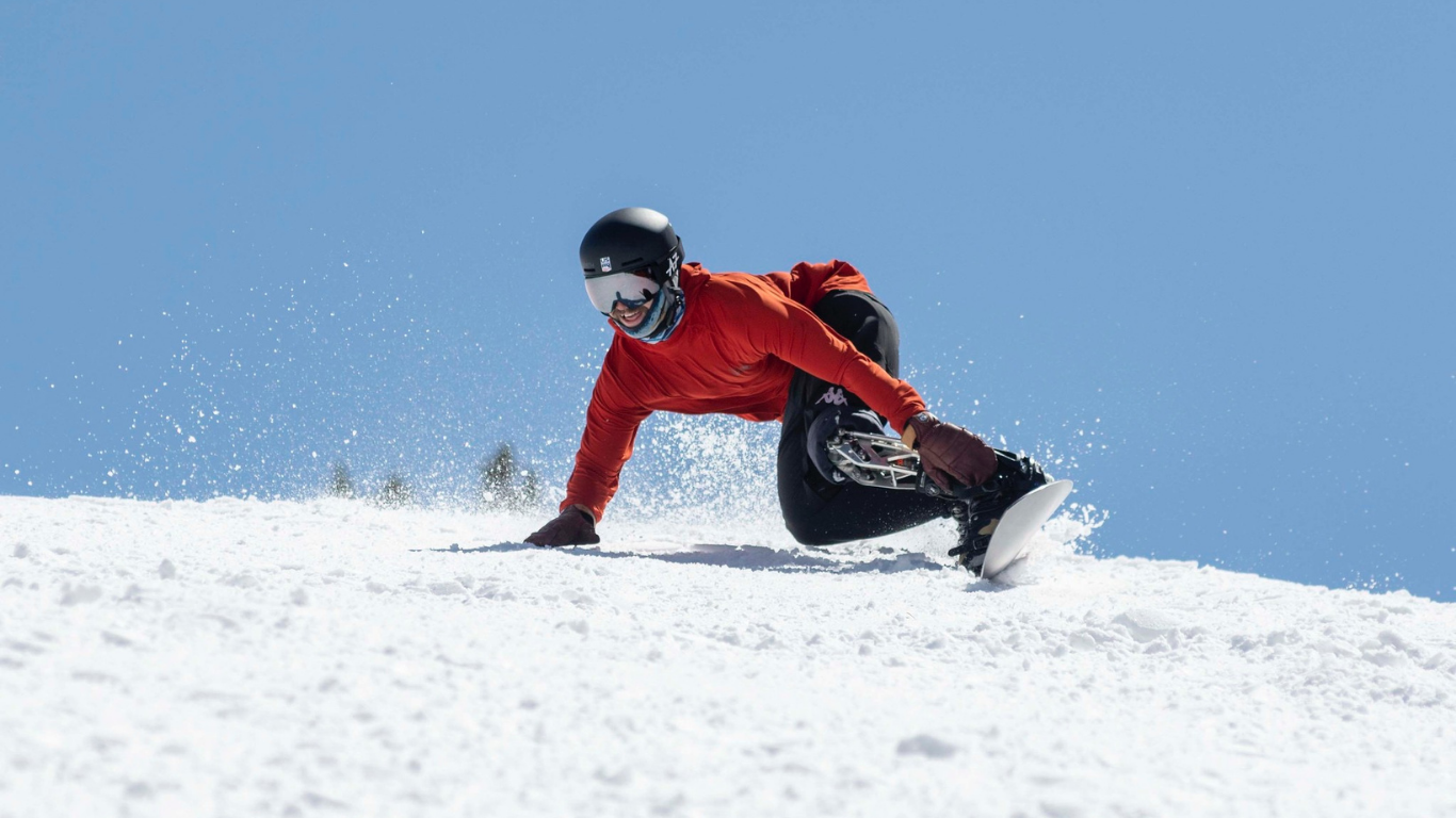 Man in red ski jacket taking an aggressive turn on a snowboard with his hand in the snow