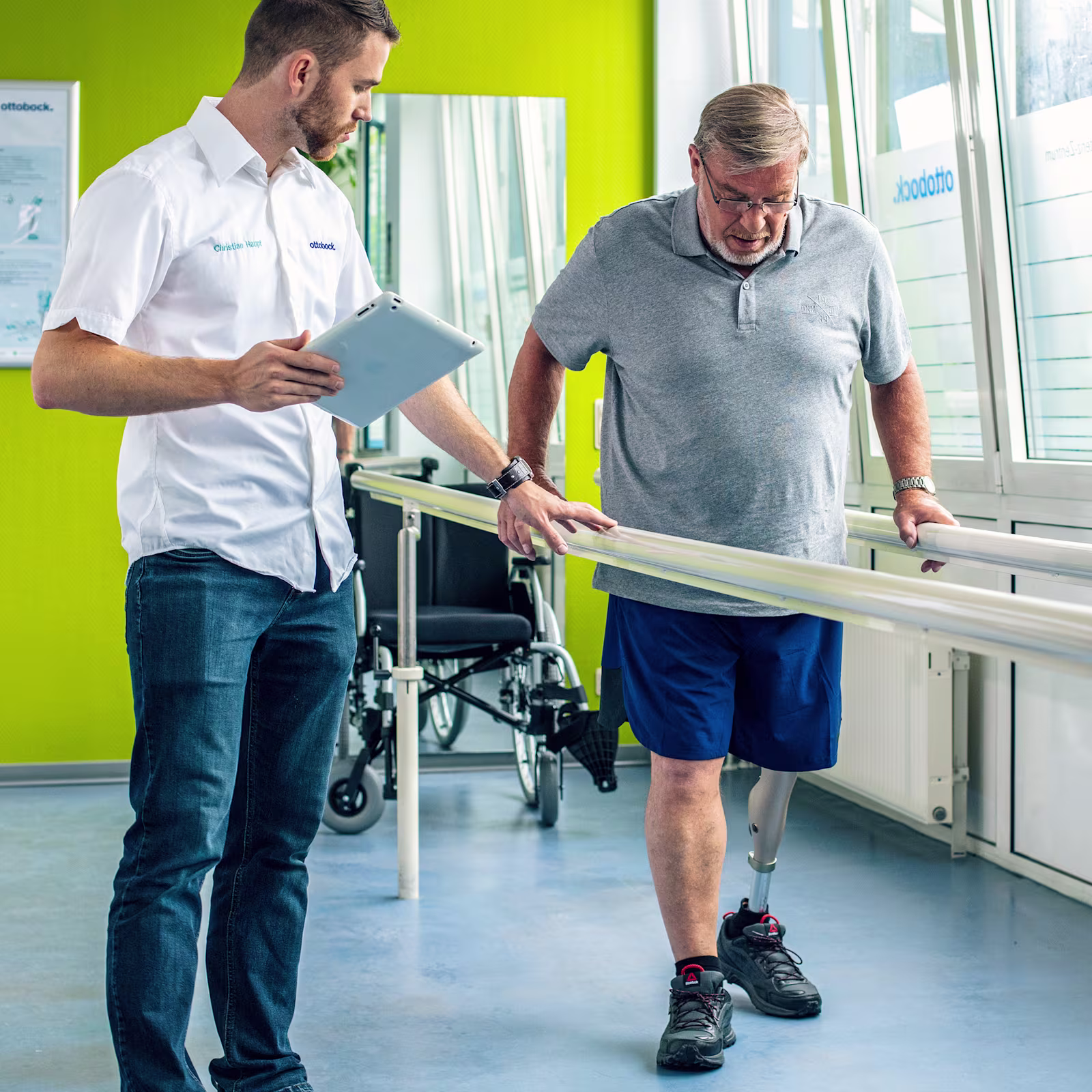 Leg amputee with Ottobock Kenevo microprocessor knee at gait training getting instructions from a prosthetist holding a tablet
