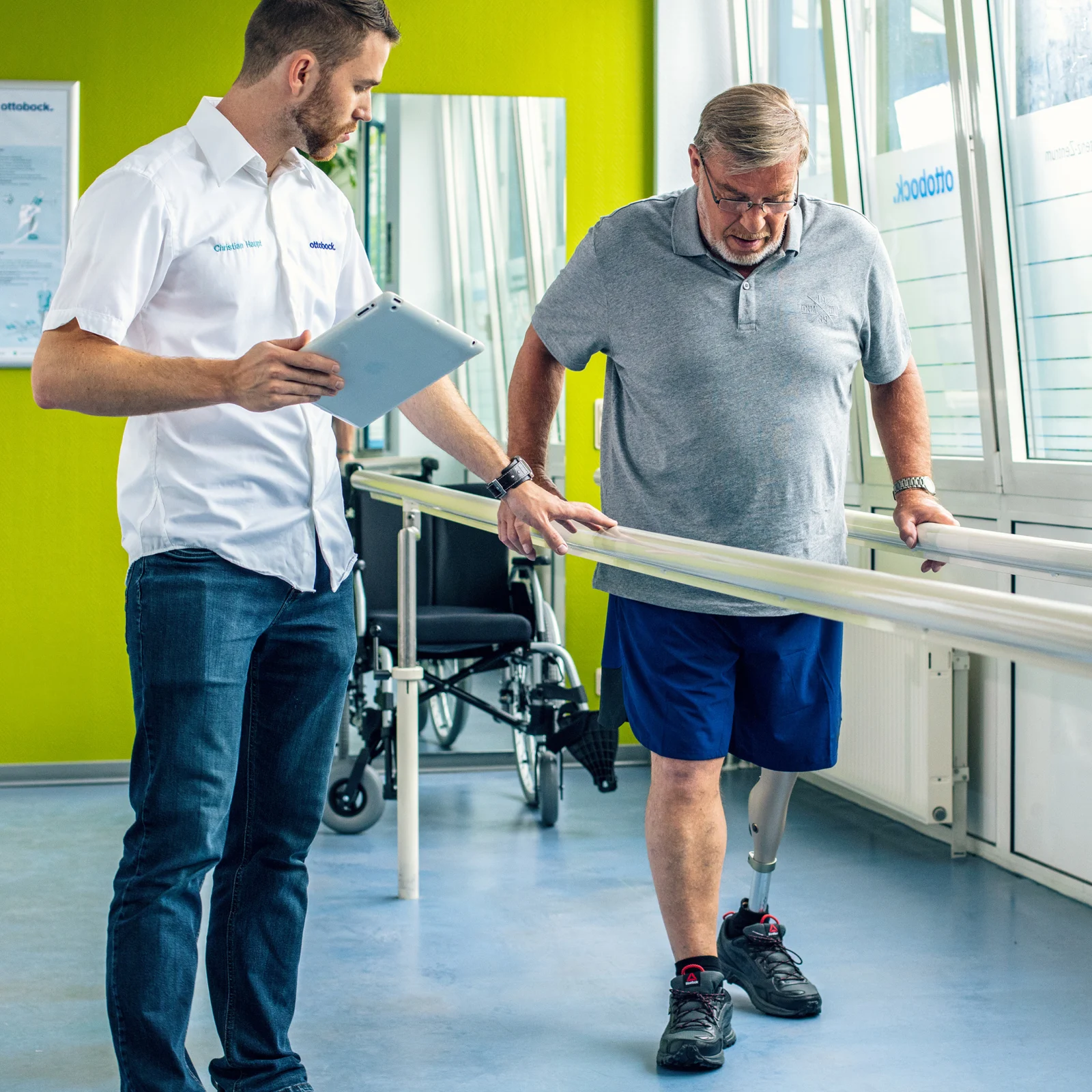 Leg amputee with Ottobock Kenevo microprocessor knee at gait training getting instructions from a prosthetist holding a tablet