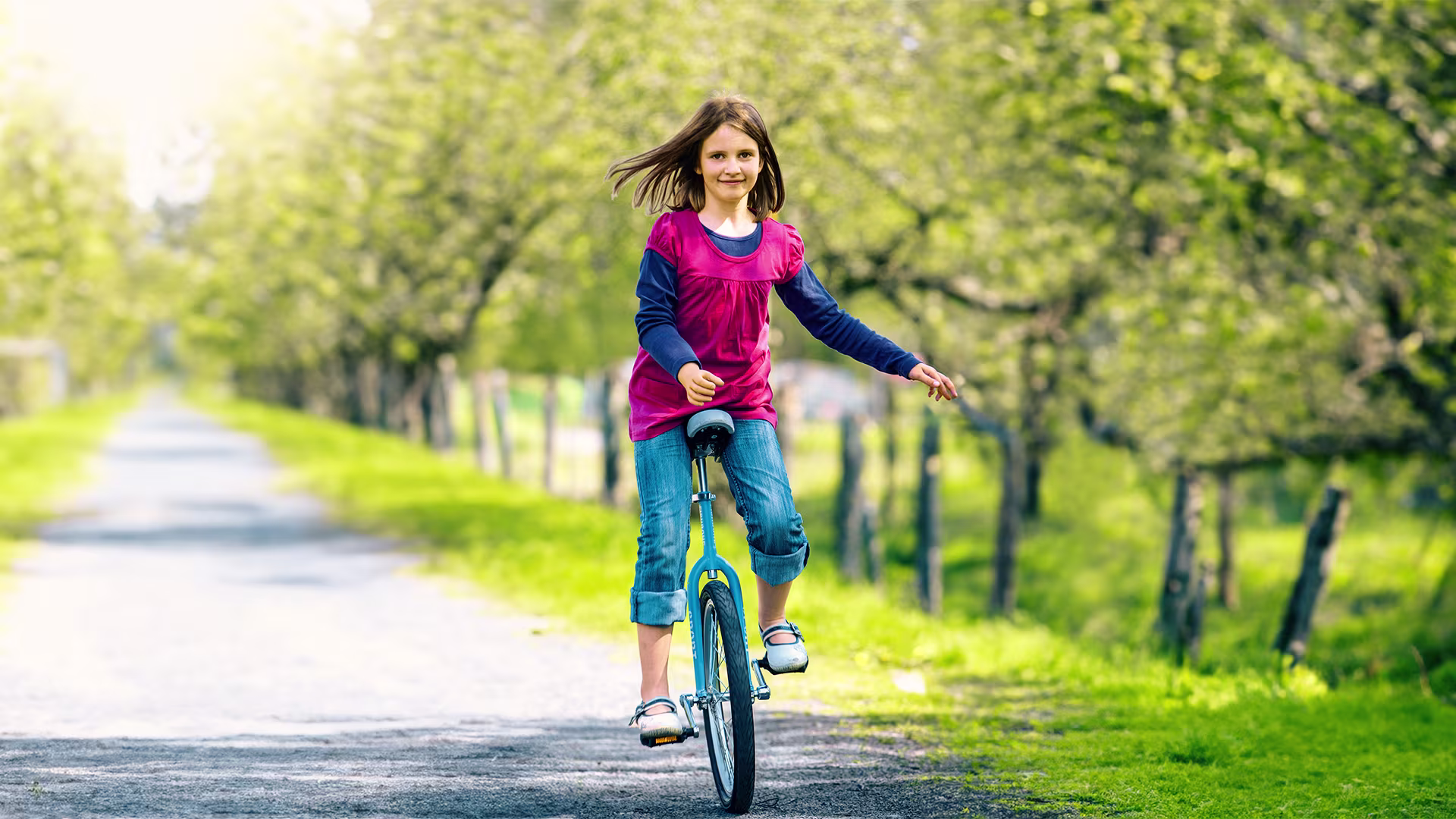 Girl with an Ottobock hand prosthesis riding a bicycle outdoors.