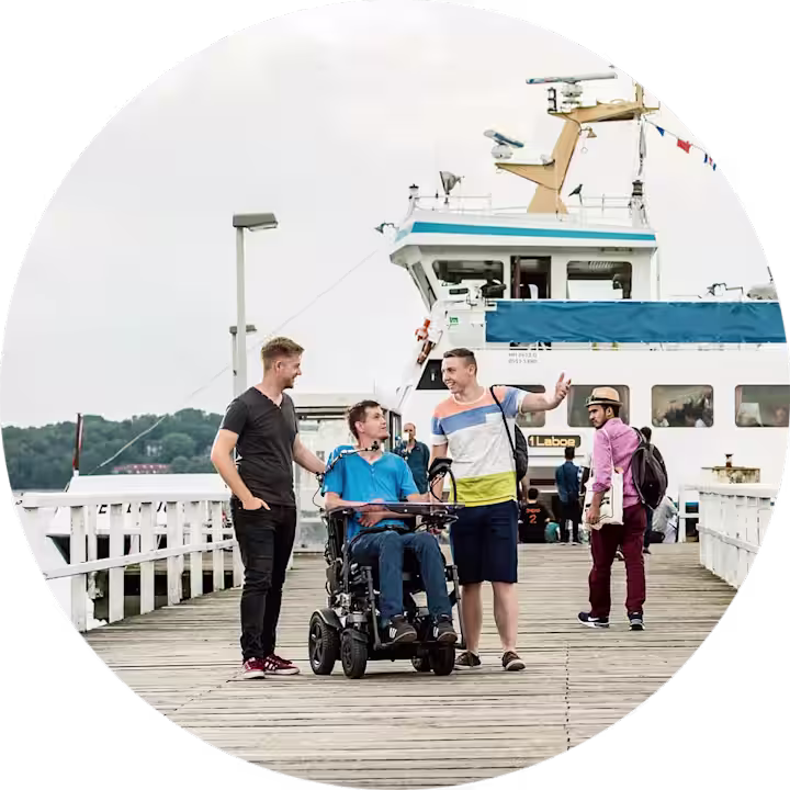 Man sieht einen Mann und zwei weitere männliche Personen rechts und links von ihm auf einer Seebrücke.