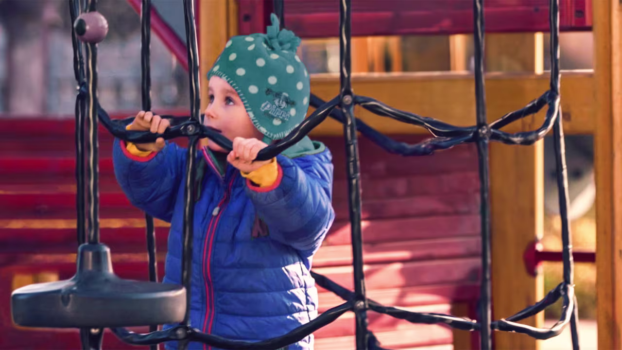 Eine junge Prothesenträgerin spielt alleine an einem Klettergerüst. Sie trägt die Elektrohand 2000 von  Ottobock.