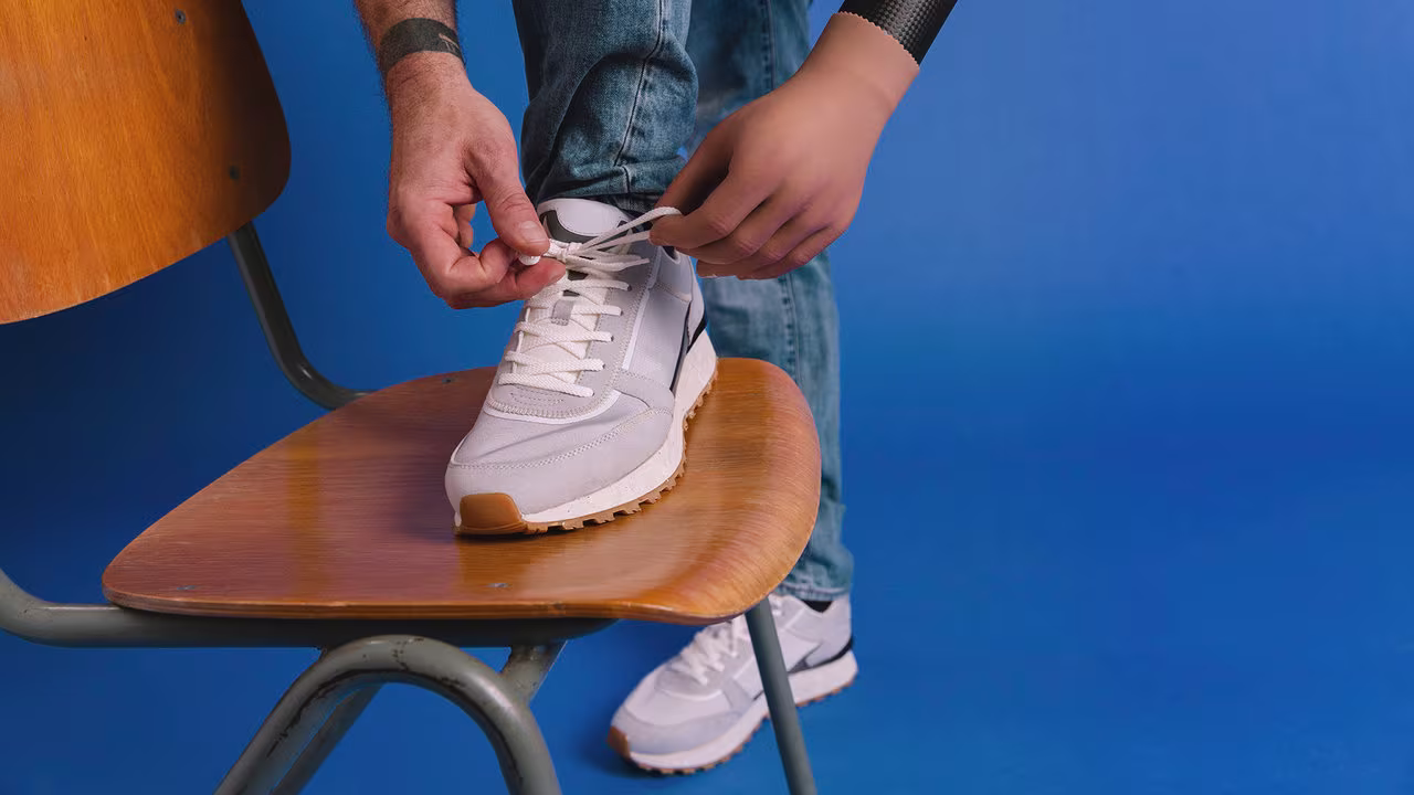Ein Prothesenträger bindet sich die Schuhe auf einem Stuhl. Er trägt die Michelangelo Hand von Ottobock.