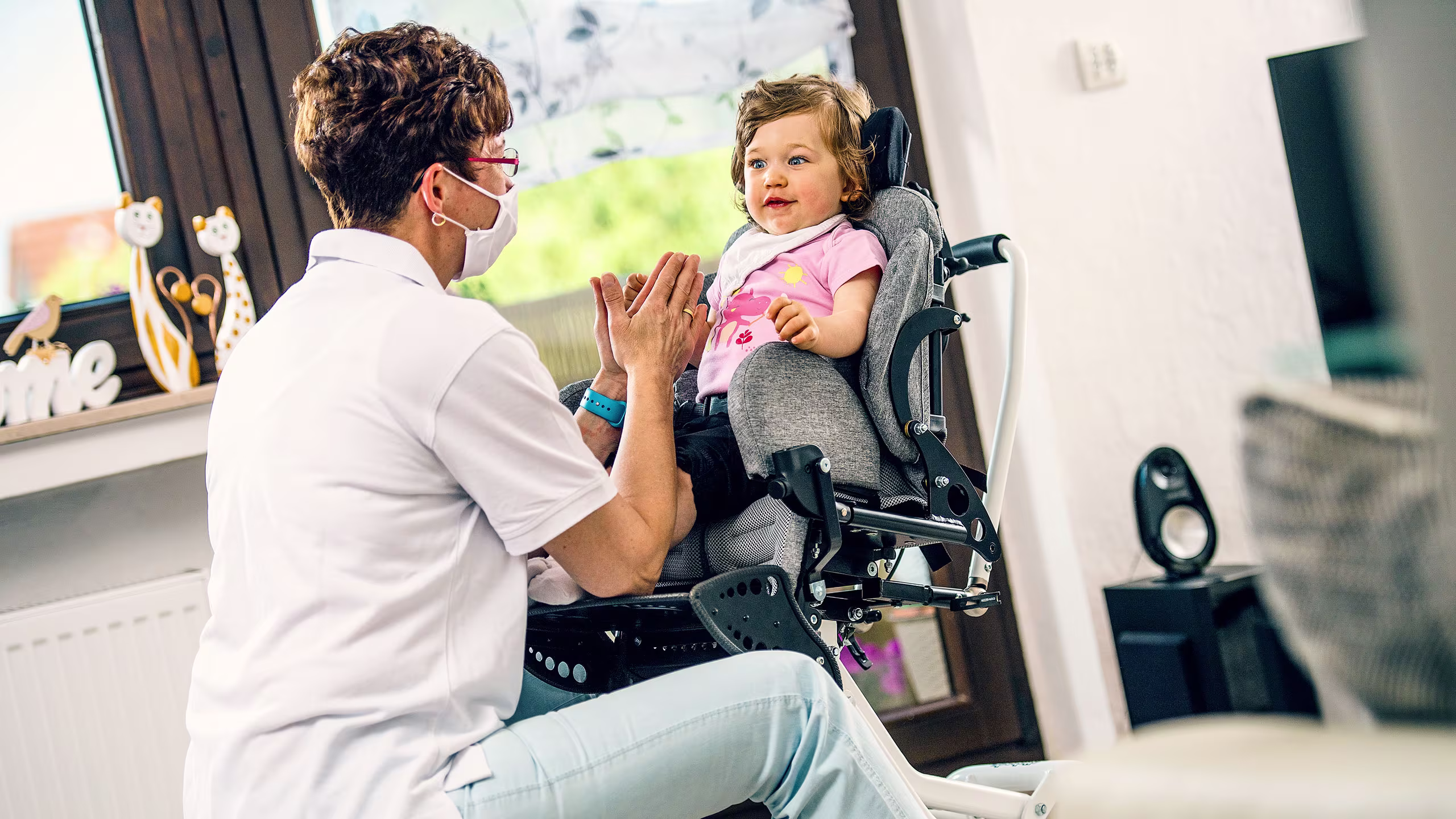 Adulto che interagisce con il bambino in una sedia Ottobock specializzata vicino ad una finestra.