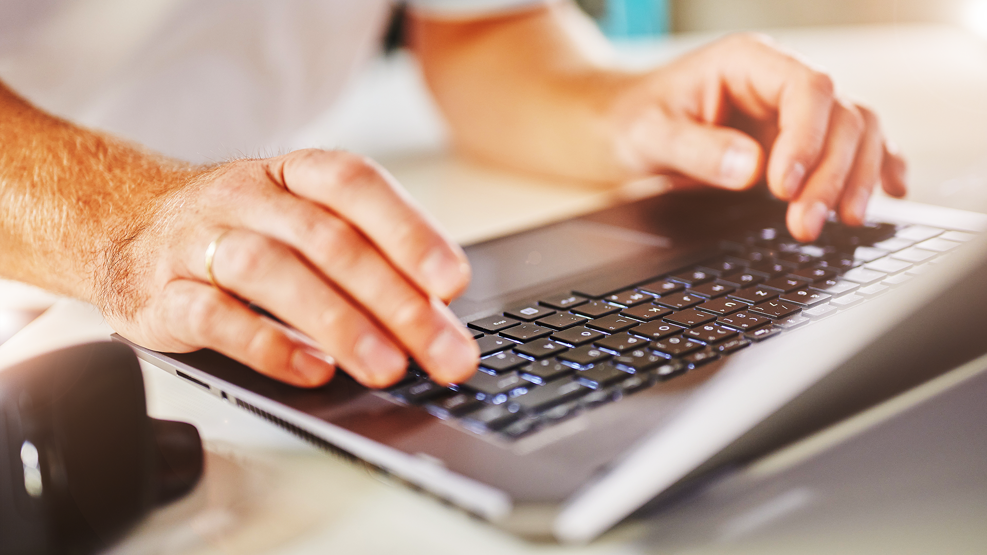 In dem Bildausschnitt sind zwei Männerhände zu sehen, die auf einer schwarzen Laptoptastatur tippen.
