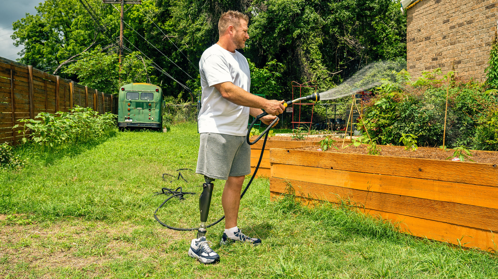 A C-Leg user is standing watering a flower bed with a hose pipe.