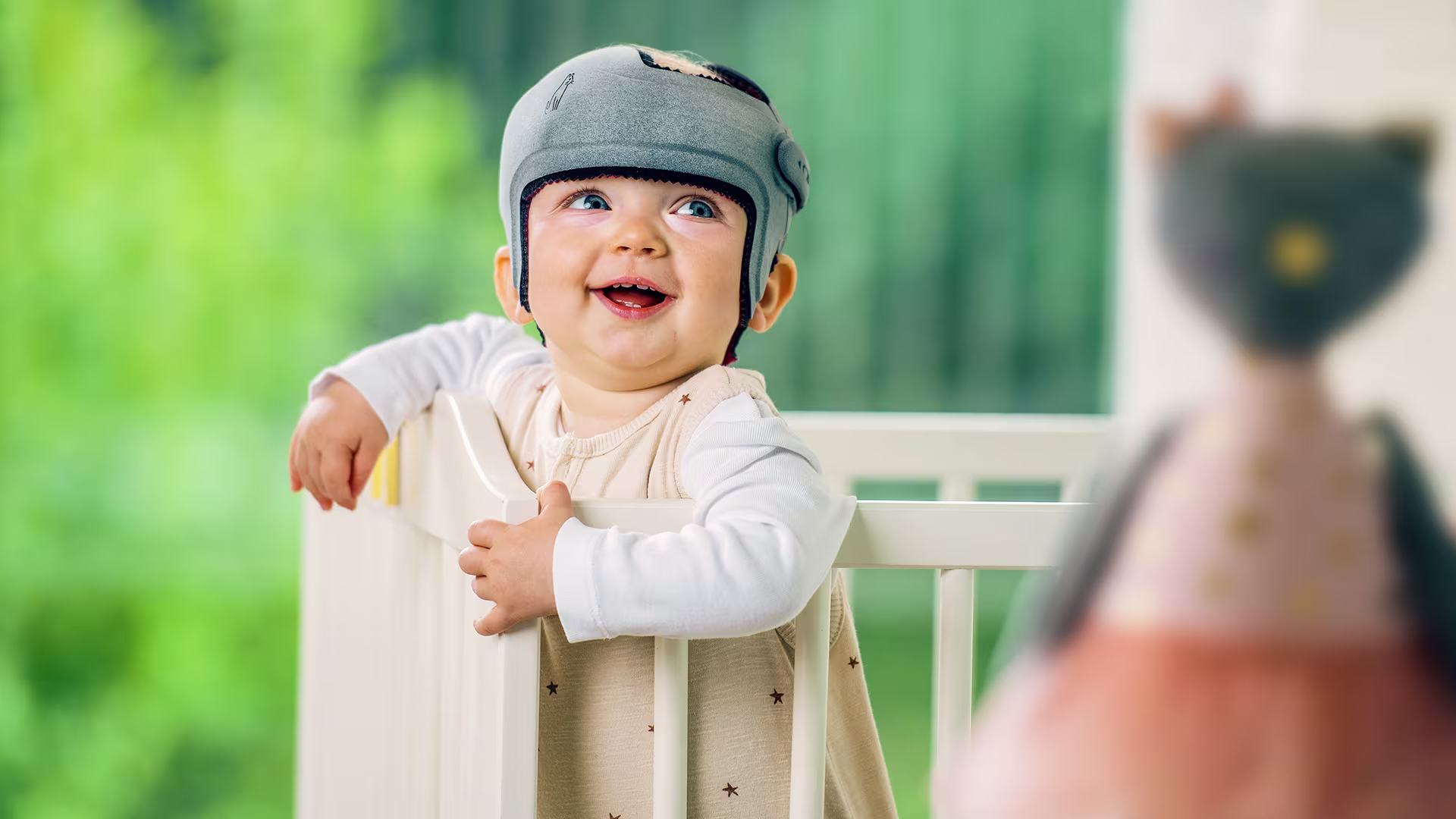 Happy baby standing in cradle wearing Ottobock’s MyCRO Band cranial remolding orthosis.