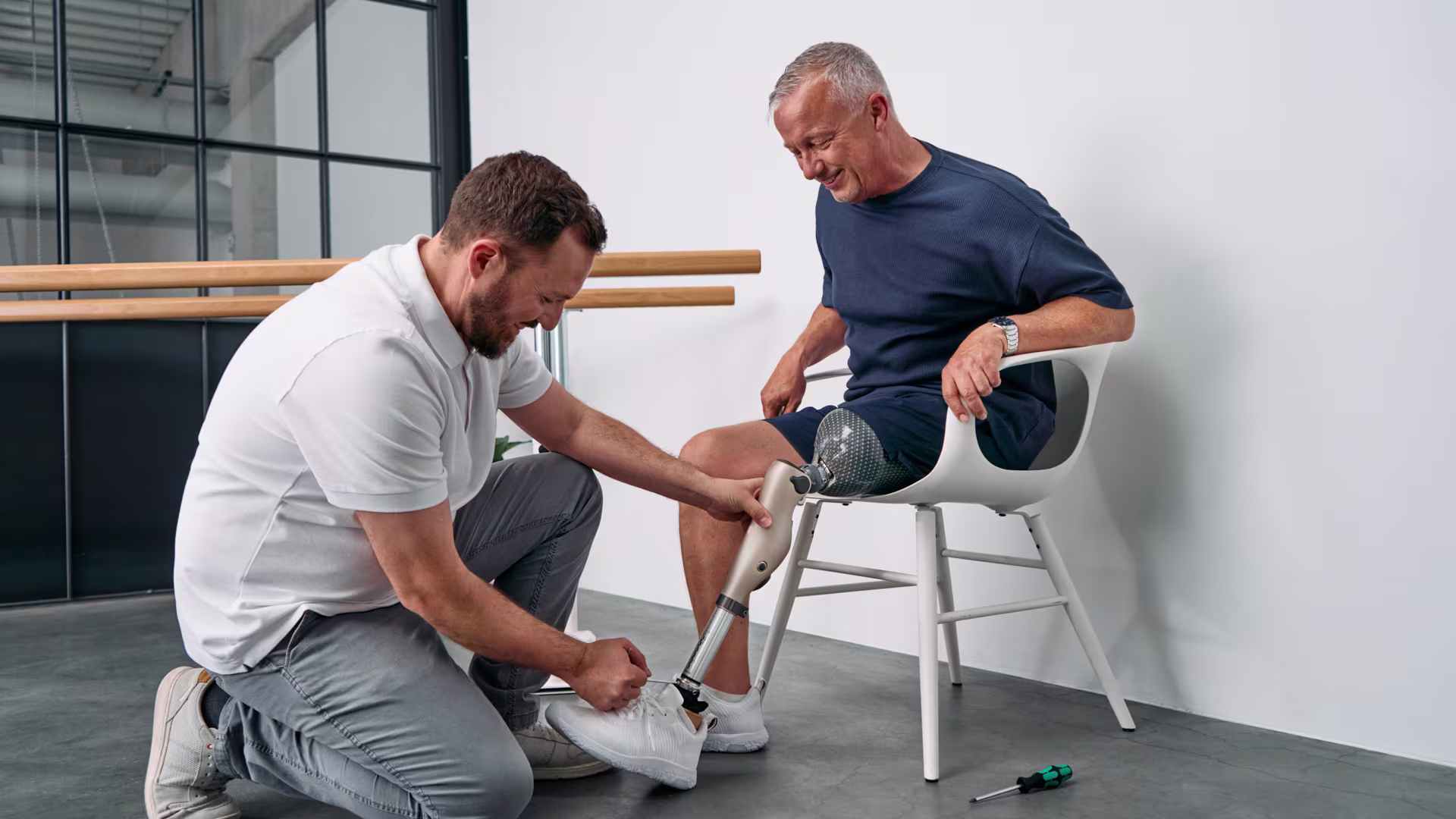 Ein Orthopädietechniker kniet vor einem amputierten Mann, und passt das mechatronische Kniegelenk Kenevo von Ottobock an.