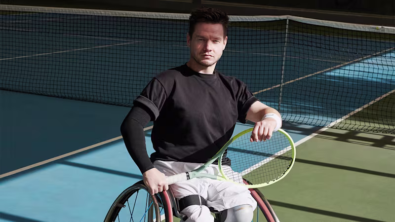 Wheelchair tennis pro in Ottobock Invader wheelchair poses with tennis racket in front of the net on an indoor tennis court