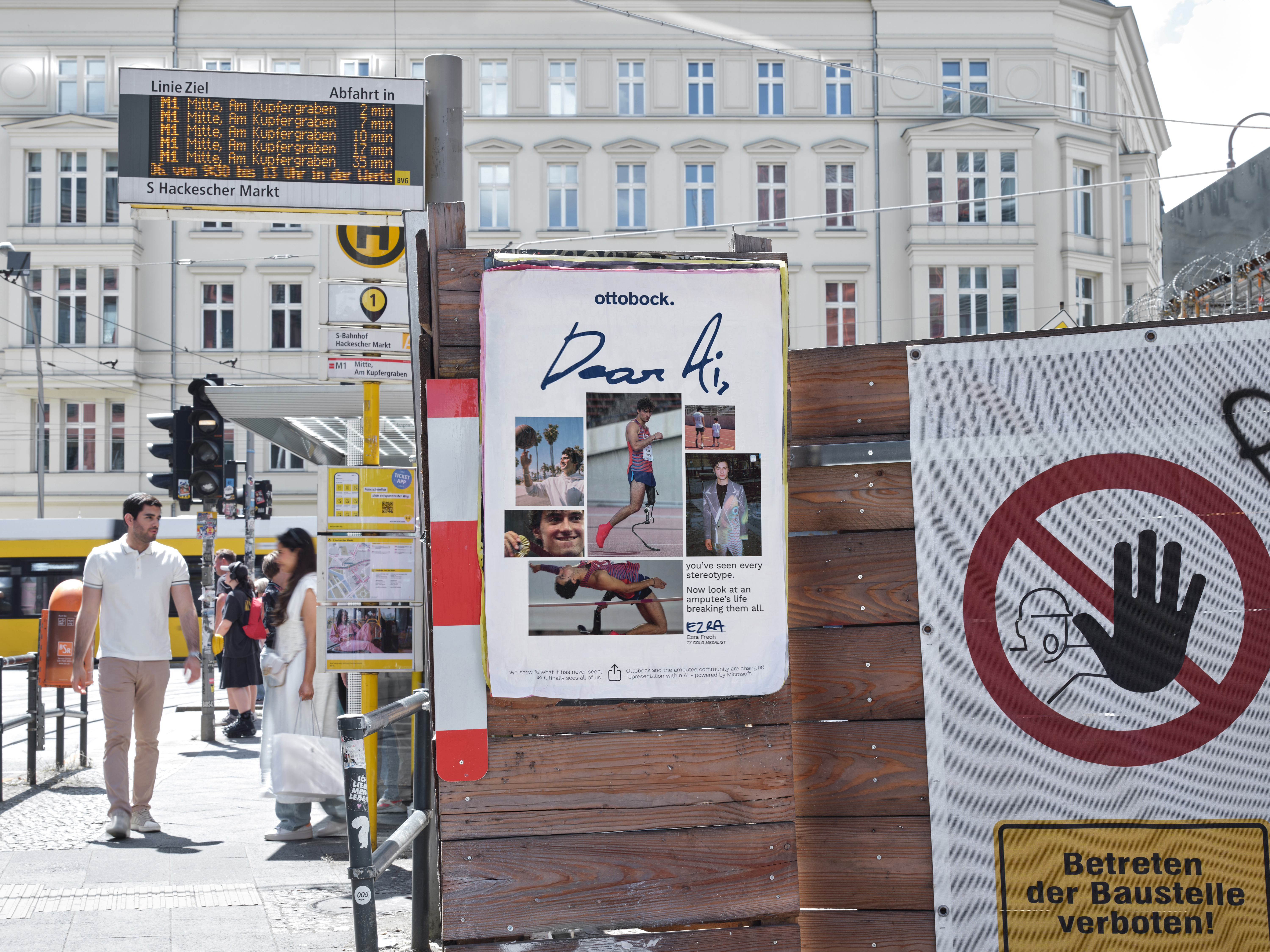 Ein Werbeplakat der Ottobock Kampagne „Dear AI“ befindet sich an einer Baustellenabsperrung am Hackeschen Markt in Berlin. Im Hintergrund sind die Haltestellenanzeige, Passanten und die historische Berliner Architektur zu sehen. Das Motiv verbindet künstliche Intelligenz, Inklusion, Barrierefreiheit und urbane Kommunikation im öffentlichen Raum.