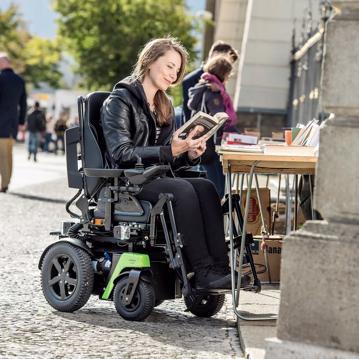 Rollstuhlfahrerin Kristina sitzt im Ottobock Juvo B4 an einem Bücherstand an der Straße und liest in einem Buch.