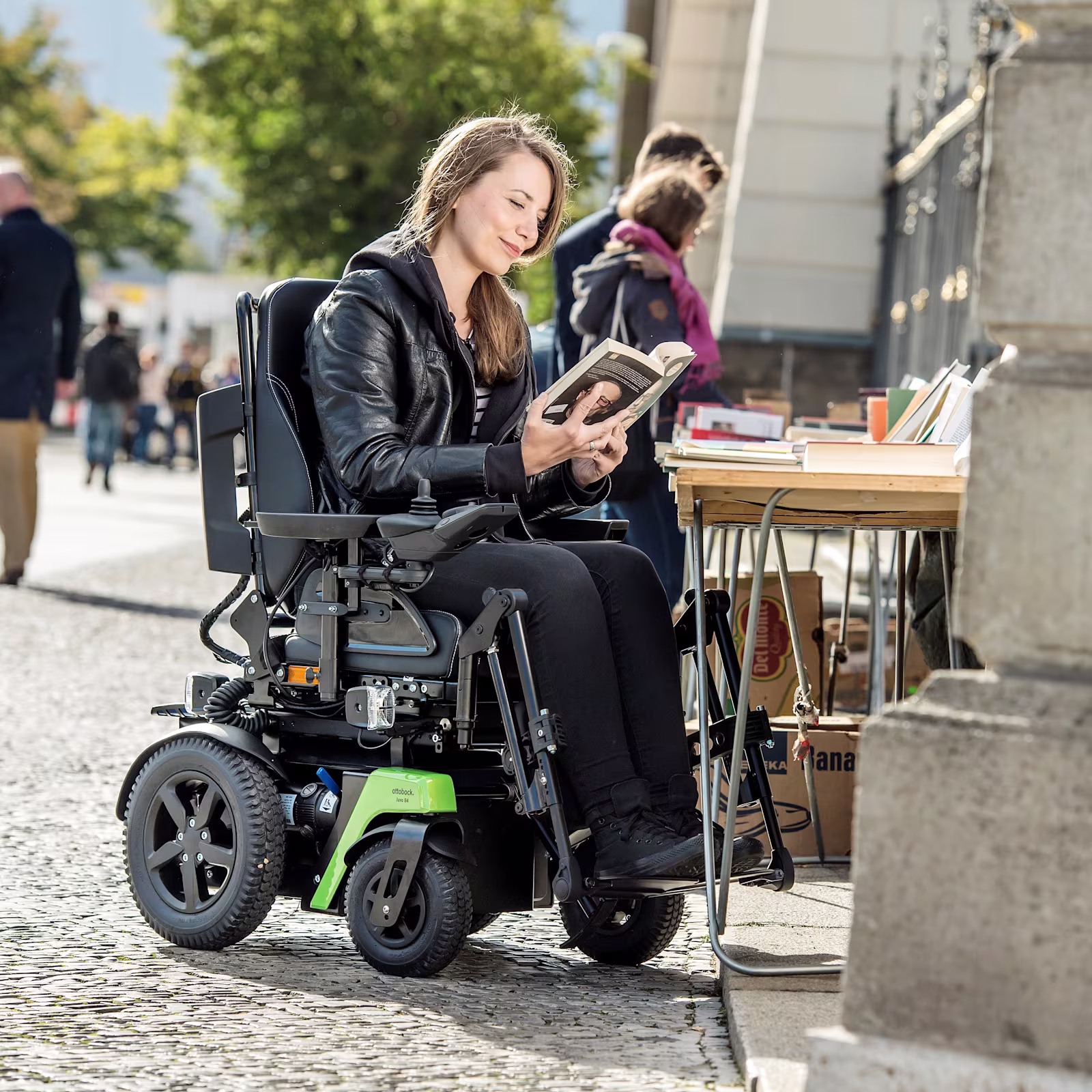 Rollstuhlfahrerin Kristina sitzt im Ottobock Juvo B4 an einem Bücherstand an der Straße und liest in einem Buch.