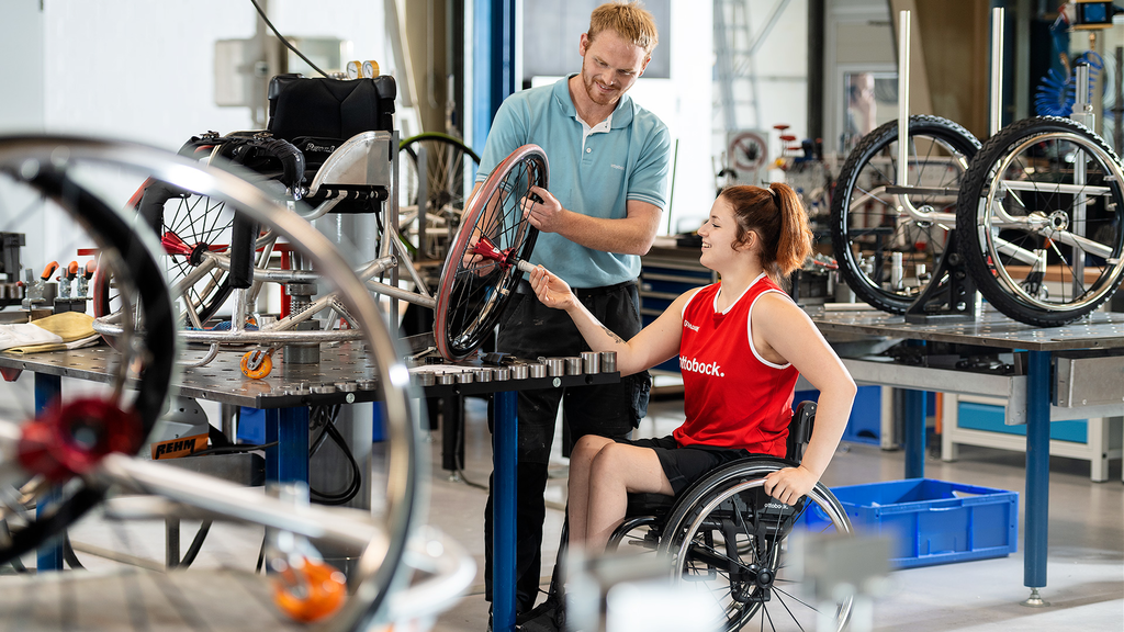 Wheelchair athlete in a workshop next to a technician looking at a wheelchair wheel