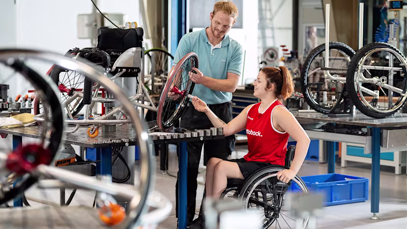Wheelchair athlete in a workshop next to a technician looking at a wheelchair wheel