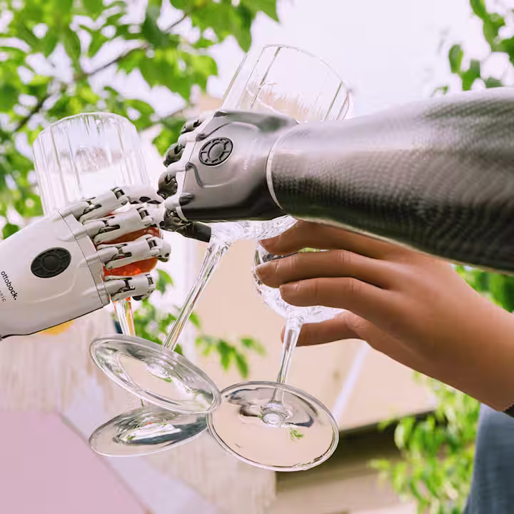 Drei Armprothesenträger halten Gläser mit Hilfe ihrer Handprothesen und stoßen damit an.