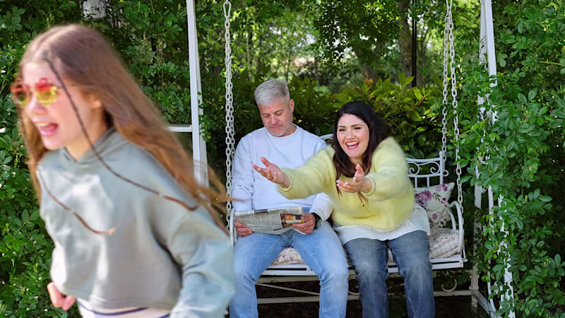 Ottobock Exopulse Mollii Suit user Elisa with family smiling in white garden swing, young girl is running and laughing