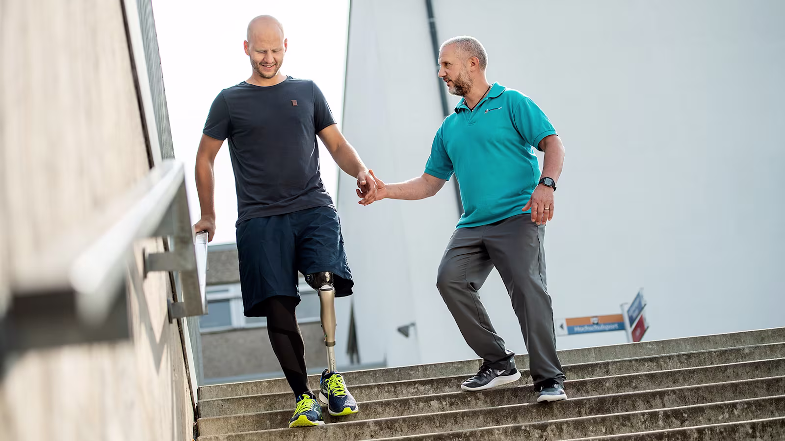 A man with a Kenevo from Ottobock walking down a set of outside stairs while being supported by his physiotherapist.