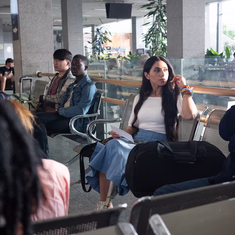 Woman with a prosthetic leg sitting in an airport waiting area, holding travel documents, representing accessibility challenges in Ottobock’s Invisible Class campaign.