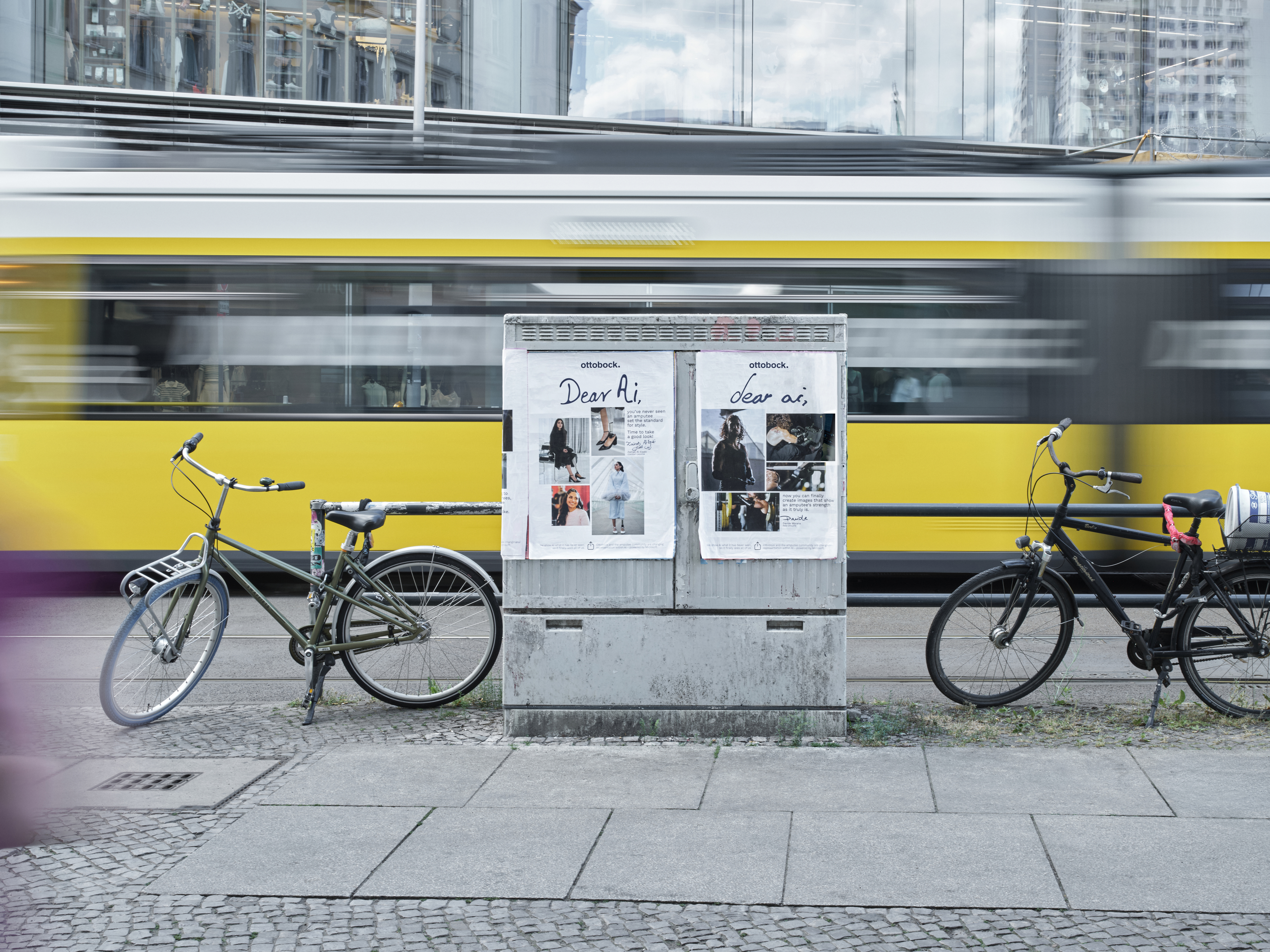 Eine gelbe Berliner Straßenbahn fährt mit Bewegungsunschärfe durch das Stadtzentrum. Im Vordergrund stehen zwei Fahrräder neben einem Schaltkasten mit Plakaten einer KI Kampagne. Die Szene verbindet urbane Mobilität, moderne Technologie, Digitalisierung und nachhaltigen Stadtverkehr in einer dynamischen Großstadtumgebung.
