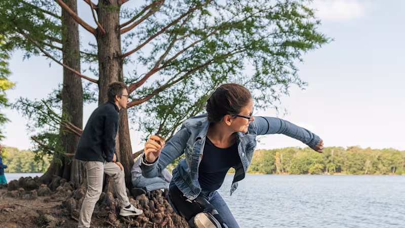 Lady wearing C-brace throwing a stone in the river.
