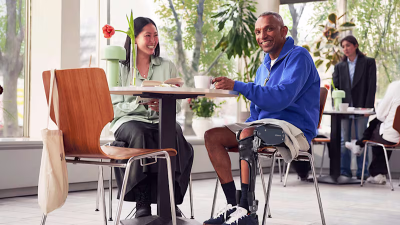 A man and a woman sit smiling at a cafe table. The man is wearing an ottobock C-Brace orthotic brace