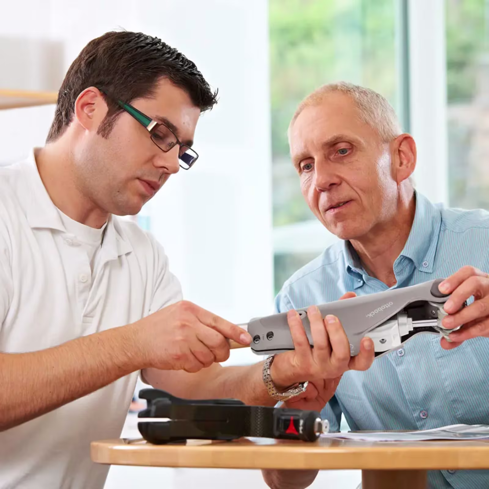 Two men sitting across a table and inspecting a prosthesis