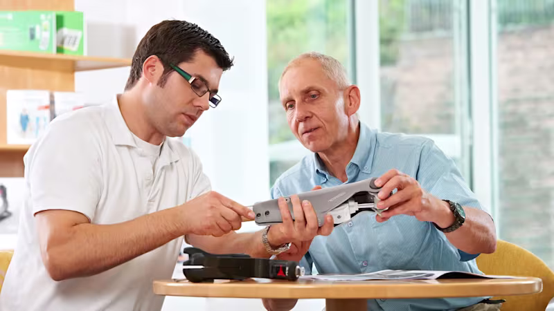 Two men sitting across a table and inspecting a prosthesis