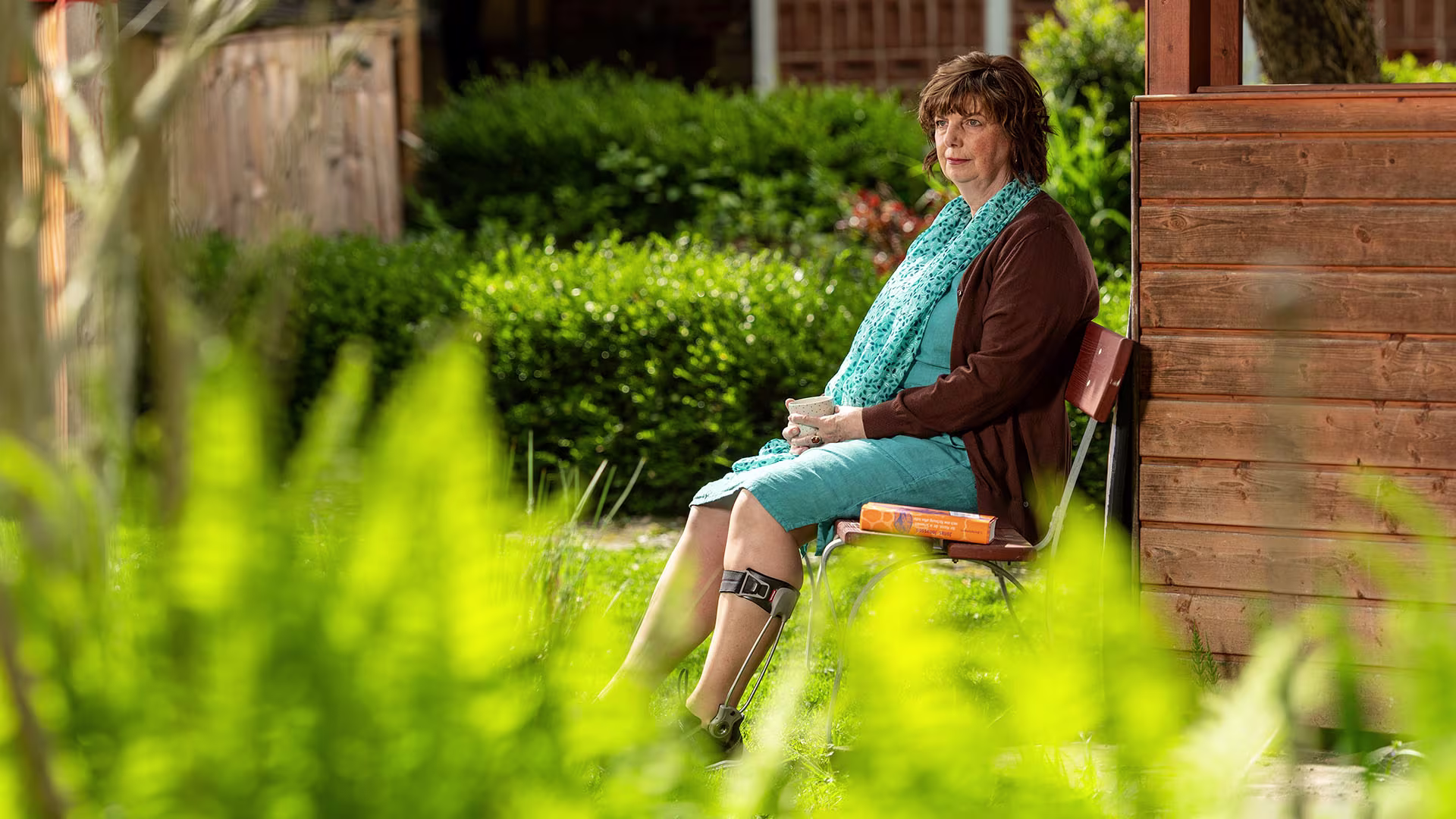 Elderly woman wearing an Ottobock Agilium Freestep sitting on a bank in the garden holding a cup