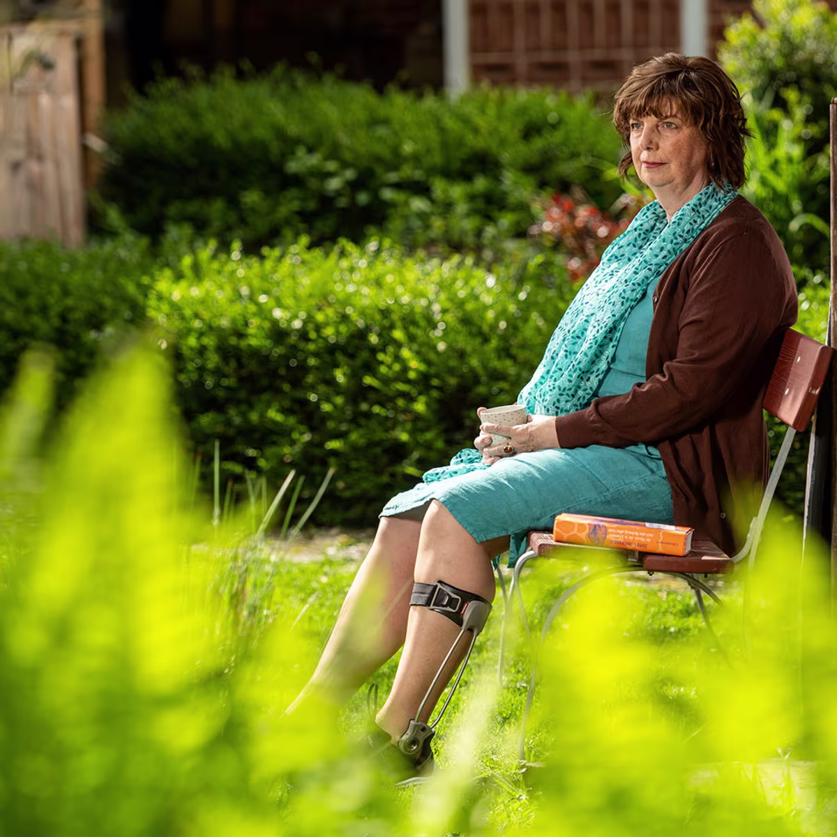 Elderly woman wearing an Ottobock Agilium Freestep sitting on a bank in the garden holding a cup