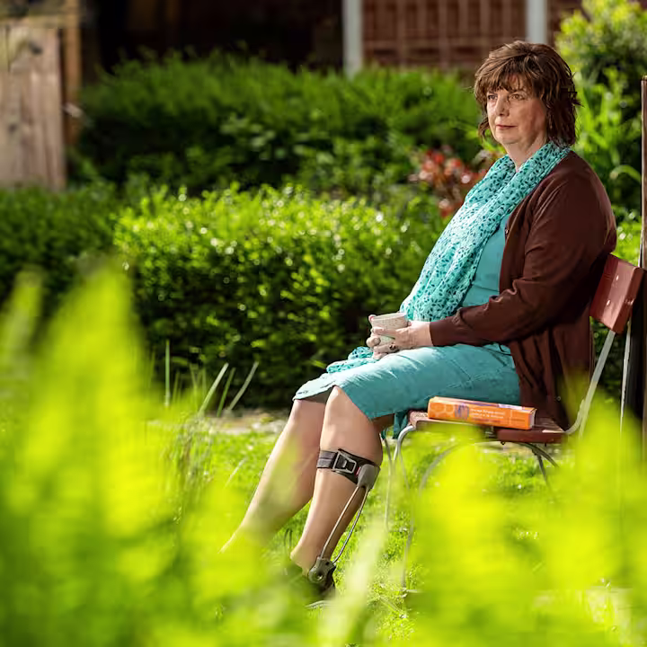 Elderly woman wearing an Ottobock Agilium Freestep sitting on a bank in the garden holding a cup