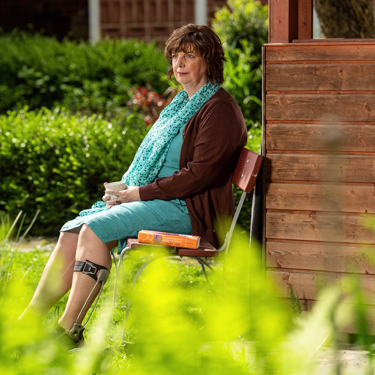 Elderly woman wearing an Ottobock Agilium Freestep sitting on a bank in the garden holding a cup