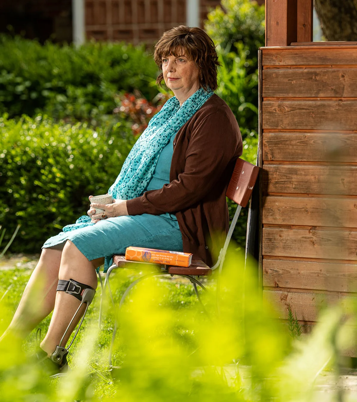 Elderly woman wearing an Ottobock Agilium Freestep sitting on a bank in the garden holding a cup