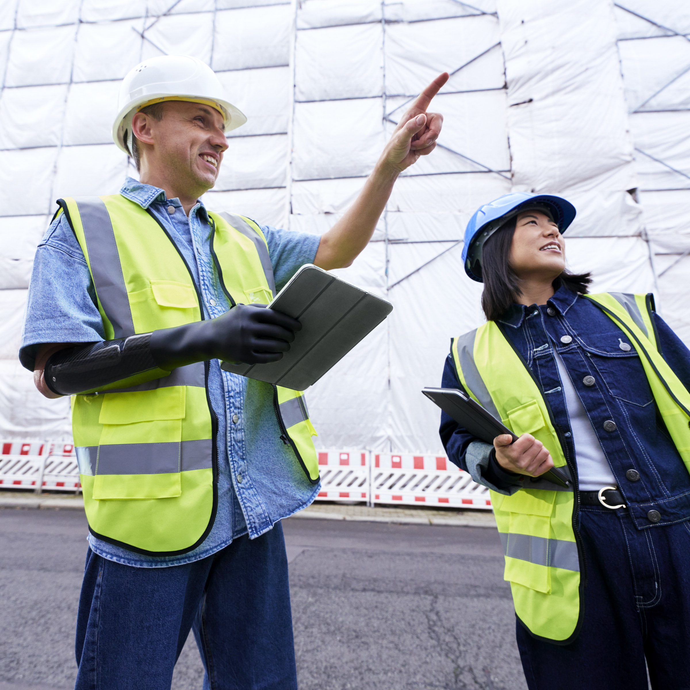 A man wearing his Ottobock michelangelo prosthetic hand is standing in front of a construction site and talking to his colleague. 
