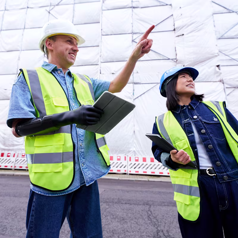 A man wearing his Ottobock michelangelo prosthetic hand is standing in front of a construction site and talking to his colleague.