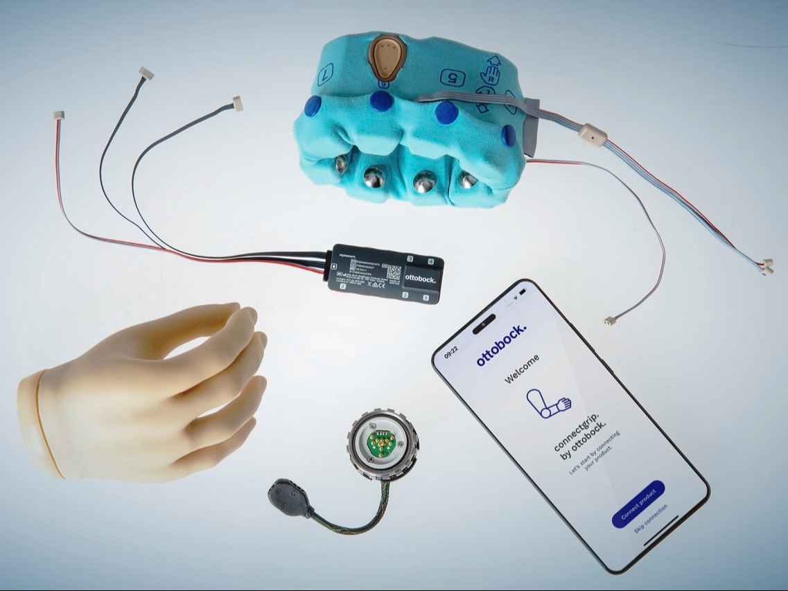 An assortment of Ottobock products scatted about, including the speedhand myoelectric prosthetic hand, the myosmart cuff prosthetic device, and a phone displaying the connectgrip app. 