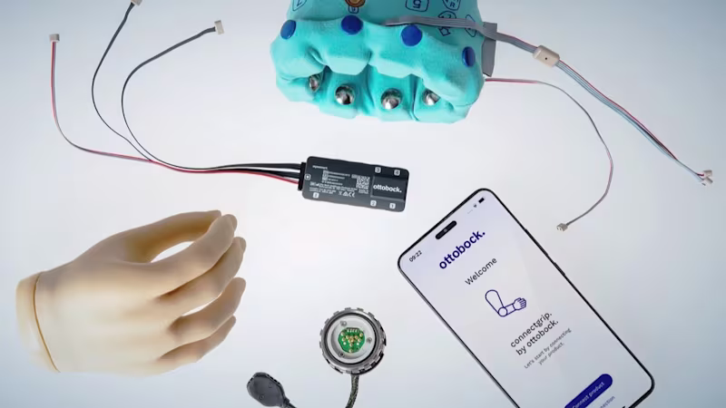 An assortment of Ottobock products scatted about, including the speedhand myoelectric prosthetic hand, the myosmart cuff prosthetic device, and a phone displaying the connectgrip app.